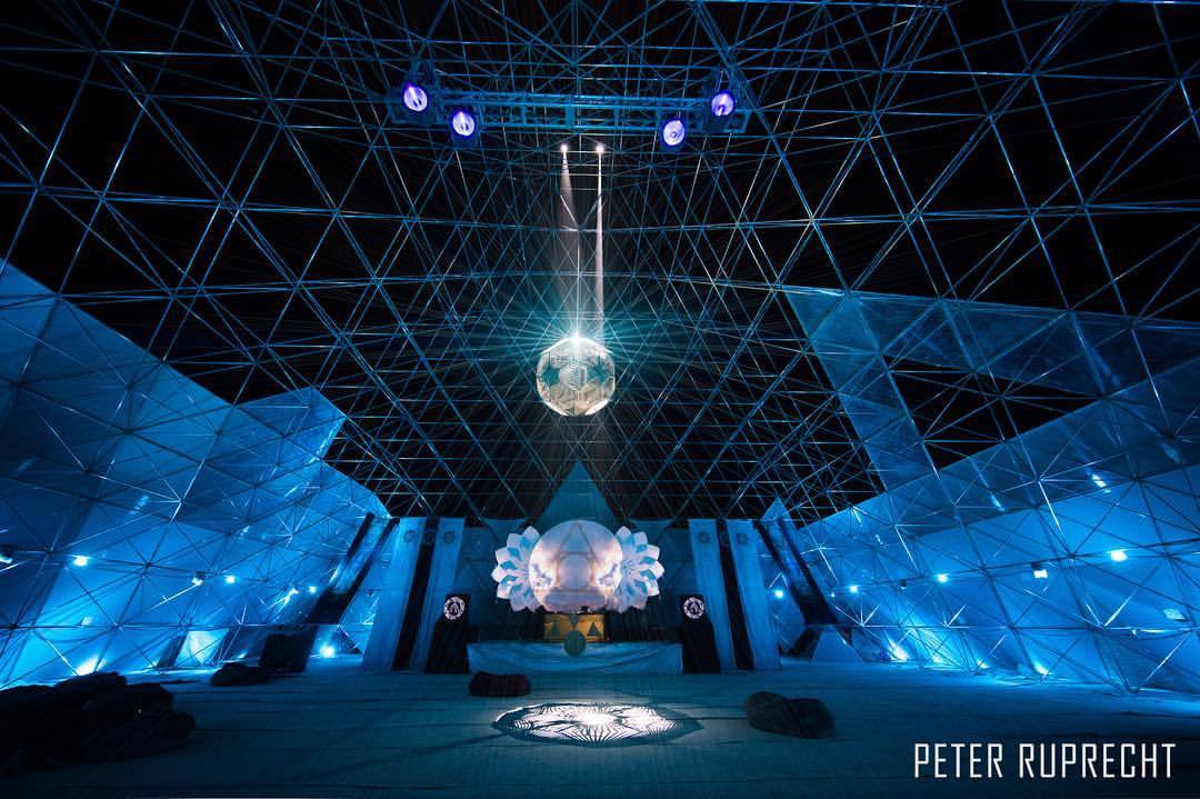 Interior of a geodesic dome art structure with stage lighting and triangular steel framework